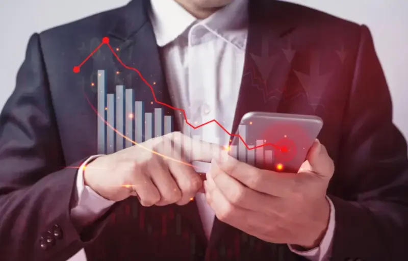 Executive holds a smartphone, with a red downward chart overlaid on the image