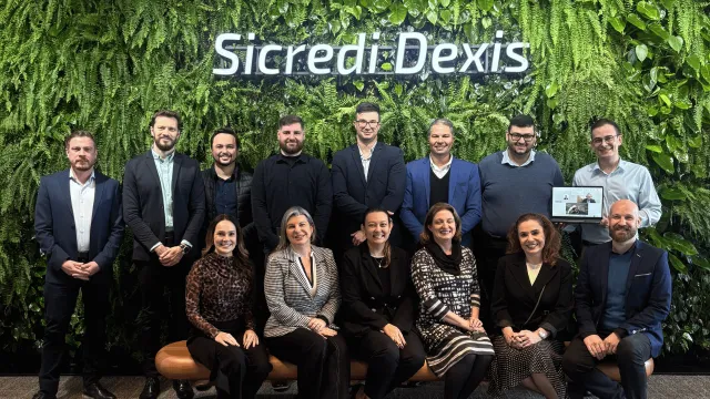 Equipo de Sicredi Dexis reunido frente a una pared verde con el nombre de la cooperativa